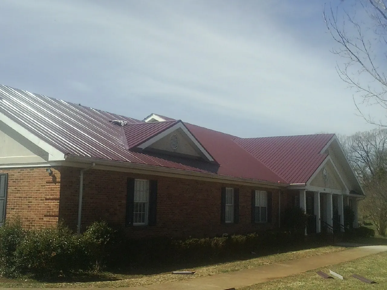 Red metal roof with gabled entries on a long brick building, from a Hail Damage Roof Repair job in Avon