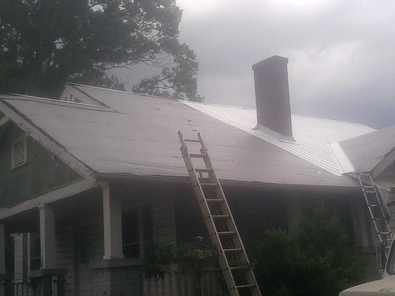 Ladders against a metal roof on an older home with a brick chimney in Avon